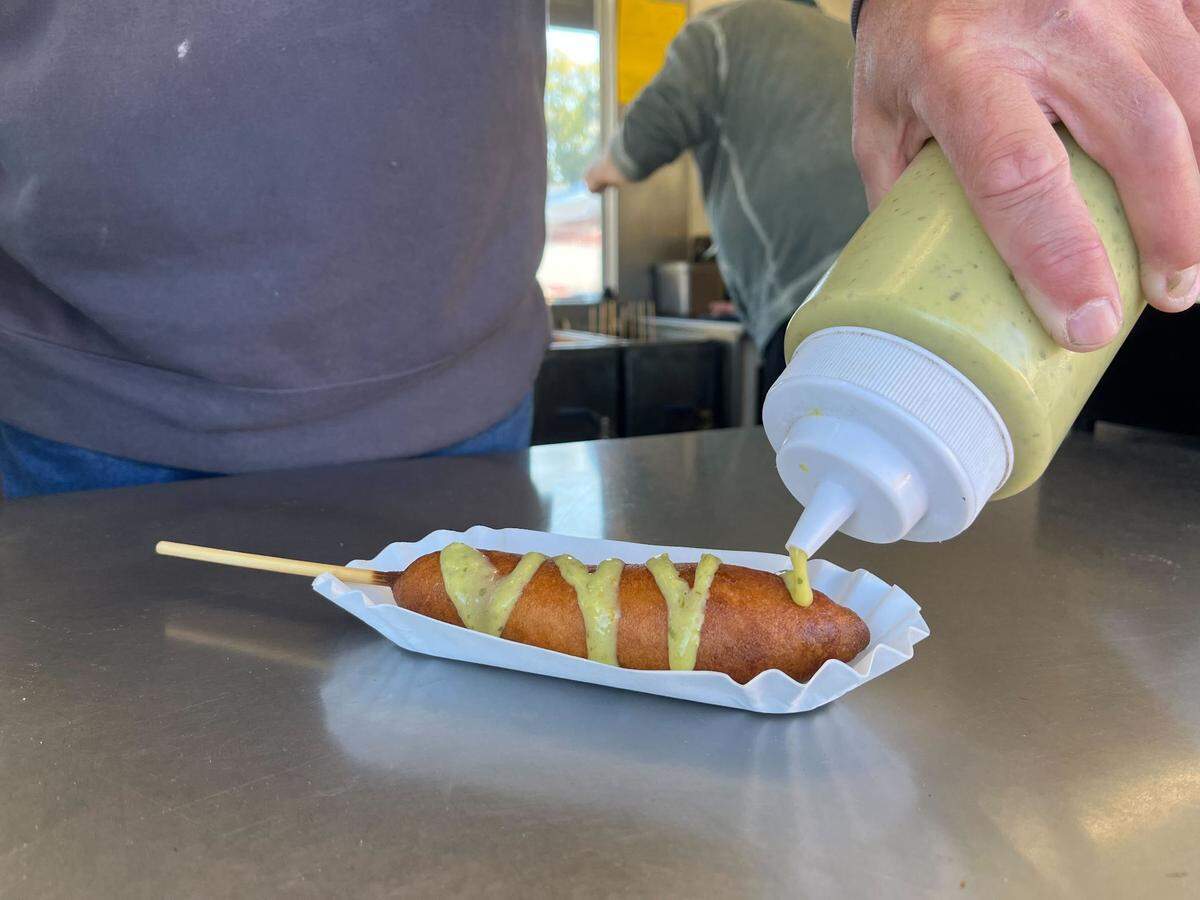 Chris Taylor, owner of the Pioneer Wagon food stand, pours “venom sauce” (avocado green chile salsa) on top of a rattlesnake corndog at the NC State Fair on Oct. 18, 2022.