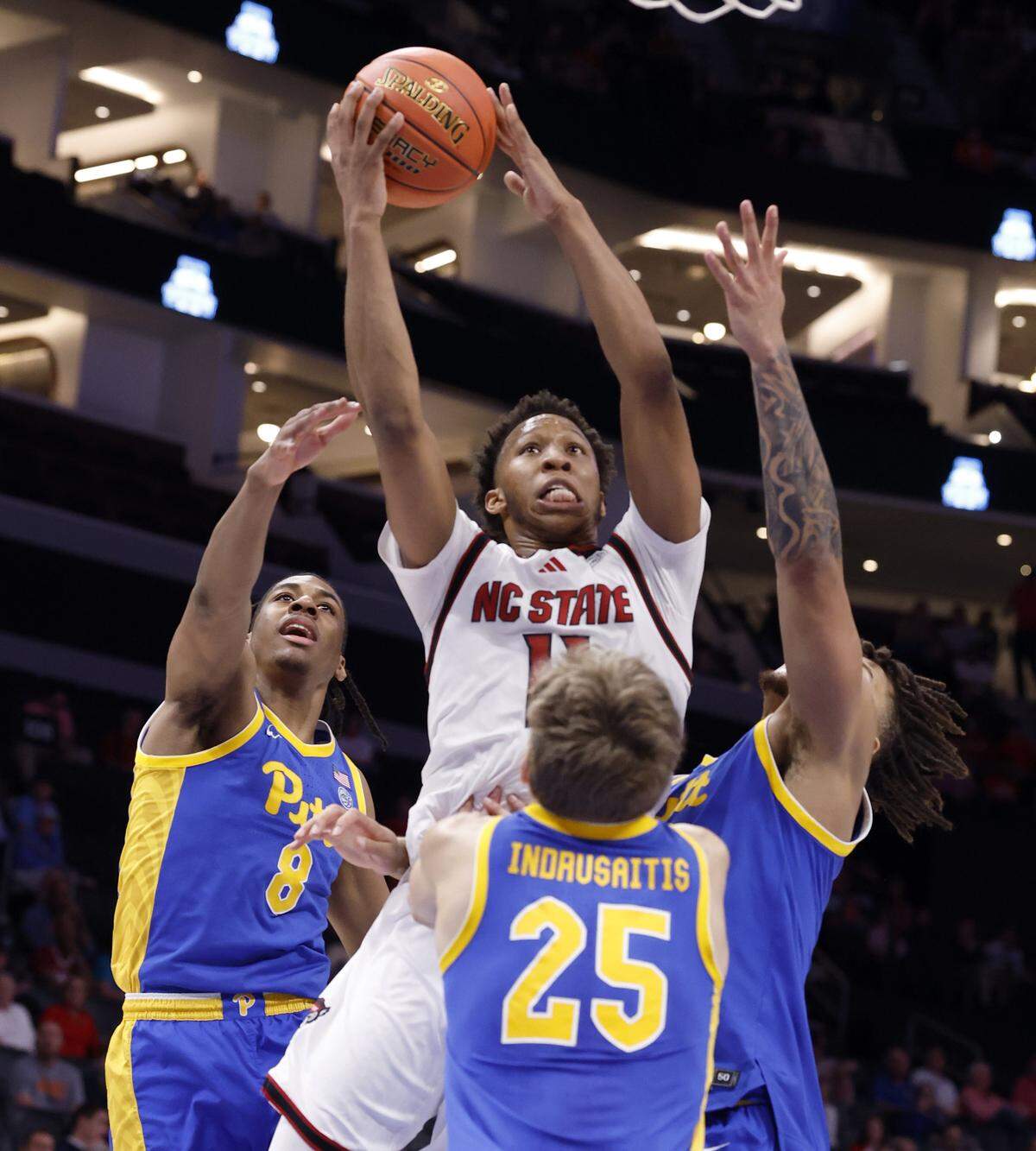 N.C. State's Quadir Copeland (11) is defended by Pitt’s Omari Witherspoon (8), Cameron Corhen (2), and Nojus Indrusaitis (25) as he heads to the basket during the first half of N.C. State’s game against Pittsburgh in the second round of the 2026 ACC Men’s Basketball Tournament at the Spectrum Center in Charlotte, N.C., Wednesday, March 11, 2026.