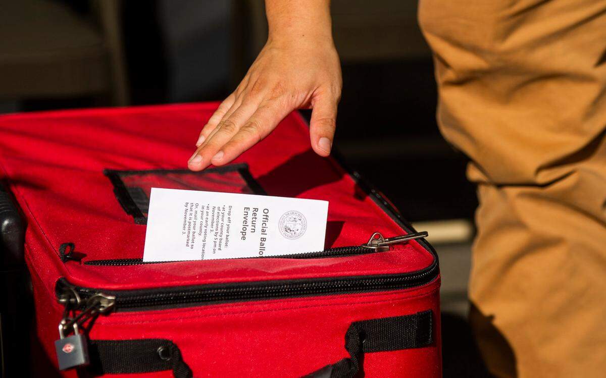 Volunteer Andrew Chang drops an absentee ballot into a locked box under a tent set up outside the Durham County Board of Elections, on Thursday, Oct. 8, 2020, in Durham, N.C.