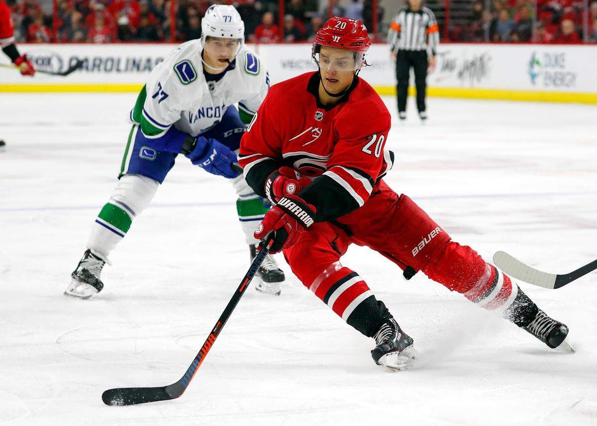 Carolina Hurricanes’ Sebastian Aho (20) gathers in the puck in front of Vancouver Canucks’ Nikolay Goldobin (77) during the second period.