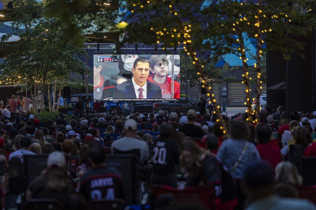 Carolina Hurricanes fans watch a large video screen during an NHL Eastern Conference Final watch party in Raleigh's Smoky Hollow district on Friday, May 29, 2026. The Hurricanes advanced to the Stanley Cup Final with a 6-1 victory over the Montreal Canadiens at Lenovo Center in Raleigh, marking the franchise's first appearance in the NHL championship series in 20 years.