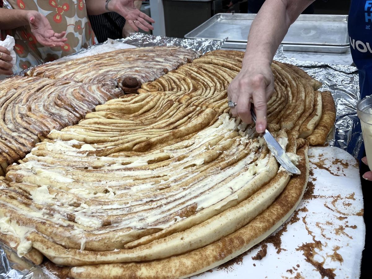 The final layer of cream cheese frosting is slathered on a giant cinnamon roll baked at St. Thomas More Catholic Church and served at SECU Family House in Chapel Hill on Friday, Oct. 4, 2024.