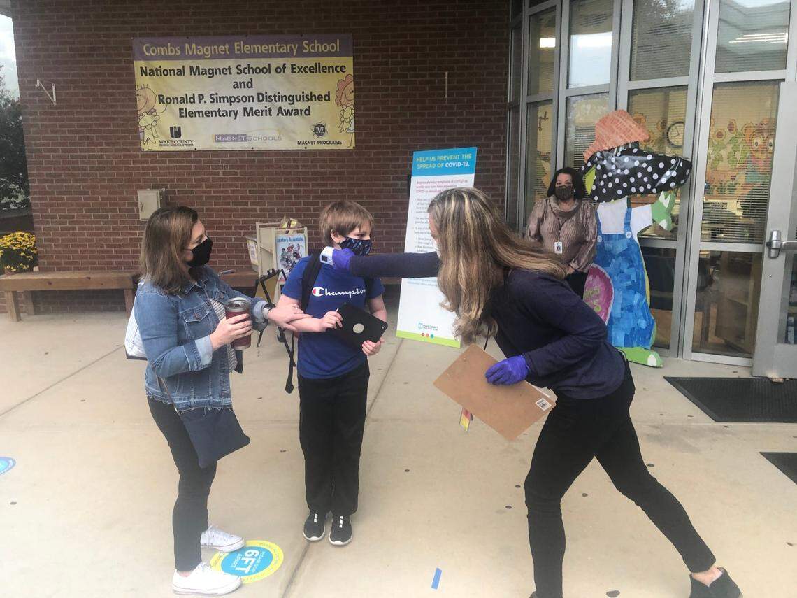 Braden Everett, a fifth-grade student, gets his temperature checked by Heather Barnes before entering Combs Elementary School in Raleigh, N.C., on Oct. 19, 2020. His mother, Paula Everett, the school’s instructional facilitator, watches.