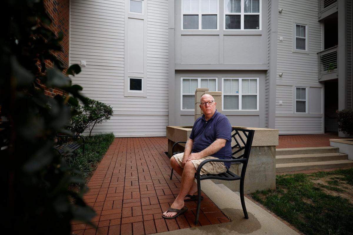 Dan Johnson, of Charlotte, N.C., sits in the courtyard near his former condo in Elizabeth Village In Charlotte, Friday, July 22, 2022. Johnson was charged cumulative $182,500 fine for a drapes violation by the homeowners association at Elizabeth Village. He contested the fine in court and has since moved from the complex.