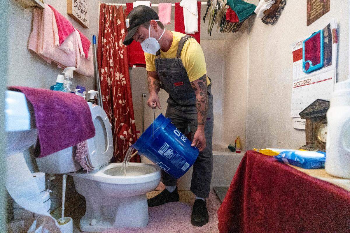 Tristan Trechsel, a volunteer with grassroots group BeLoved Asheville, flushes a toilet with gray water in a iow-income independent living facility, with no running water on Wednesday, October. 8, 2024. About half of Asheville’s water customers were still without running water this week because the remnants of Hurricane Helene ripped apart the city’s distribution system.