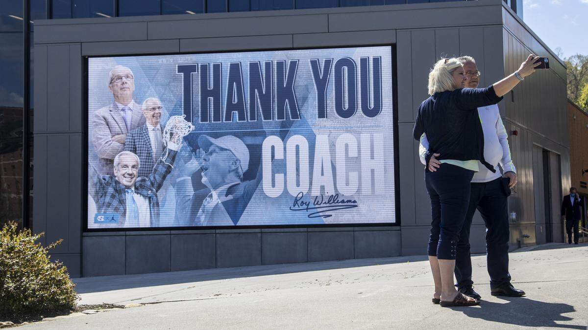 Carolina fans Cindy and Blaine Bringhust of New York pose for a selfie in front of a sign thanking mens basketball coach Roy Williams at the Dean Smith Center at UNC-Chapel Hill. Williams announced his retirement Thursday, April 1, 2021