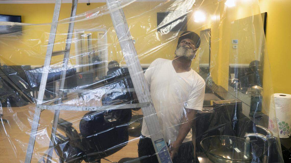 Barber Alex Walton hangs shower curtains between chairs in the Before & After Barbershop on Poole Road as he prepares to open on Friday afternoon, May 22, 2020 in Raleigh, N.C. The shop has been closed since March due to the spread of the COVID-19 virus. ‘It’s inexpensive and it gets the job done’, we’re COVID-19 ready’, Walton said.
