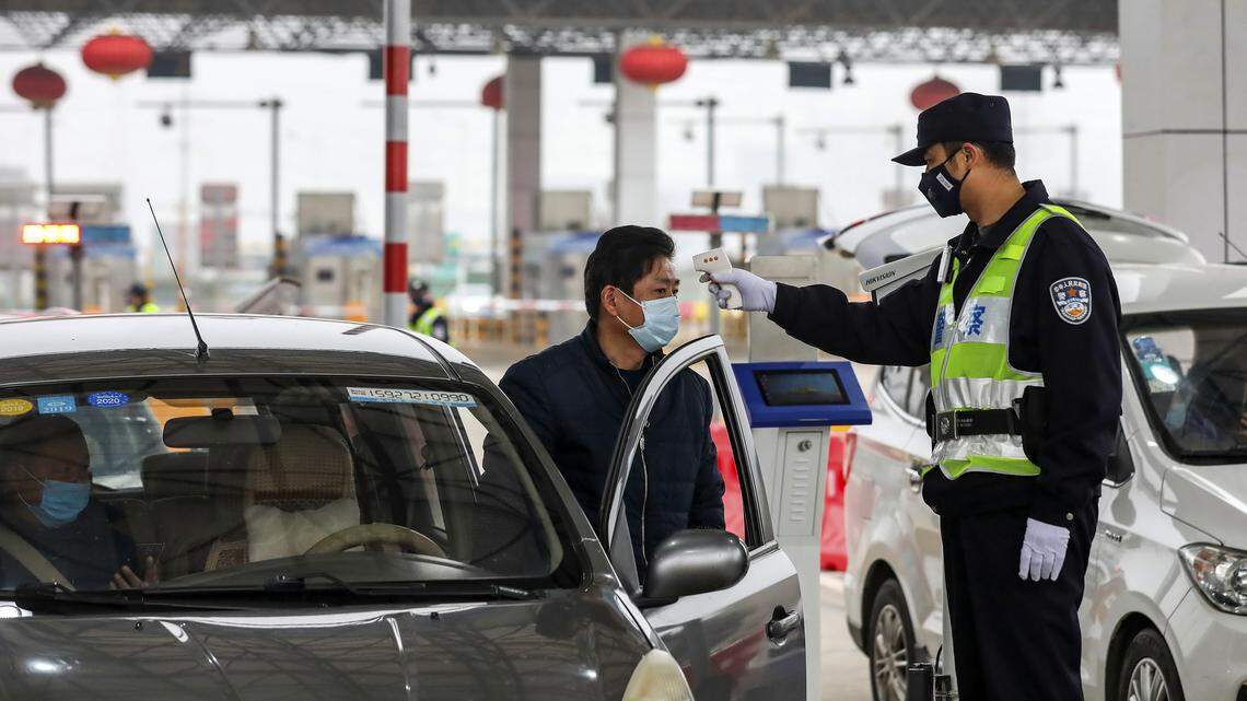 FILE - In this Jan. 23, 2020, file photo, a policeman uses a digital thermometer to take a driver’s temperature at a checkpoint at a highway toll gate in Wuhan in central China’s Hubei Province. Cutting off access to entire cities with millions of residents to stop a new virus outbreak is a step few countries other than China would consider, but it is made possible by the ruling Communist Party’s extensive social controls and experience fighting the 2002-03 outbreak of SARS.
