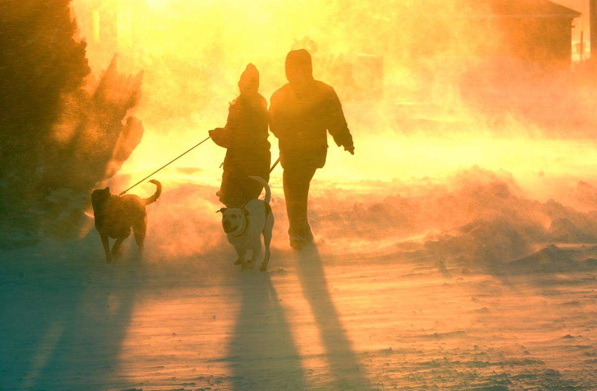Jacqueline Riddle, left, and April Whisonant walk their dogs Nikki and Fat Boy through the blowing snow as the sun sets at Kill Devil Hills after a winter storm dumped several inches of snow in January 2002.