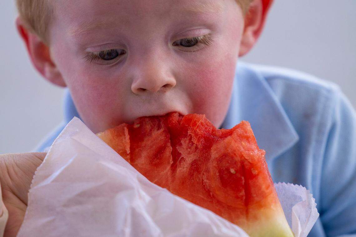 Two-year-old Myles Derrick of Plymouth eats a freshly cut slice of watermelon during the annual Watermelon Day at the North Carolina State Farmers Market, Thursday July 28, 2022.