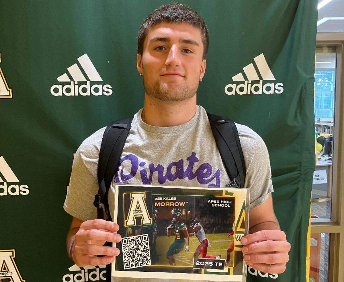 Apex High School senior Kaleb Morrow poses with a placard in his school’s library that includes a QR code with all of his recruiting information. Apex coach John Mozerka uses the placards to assist players off the radar of Division I recruiters yet with the passion to continue playing at a lower-division program.