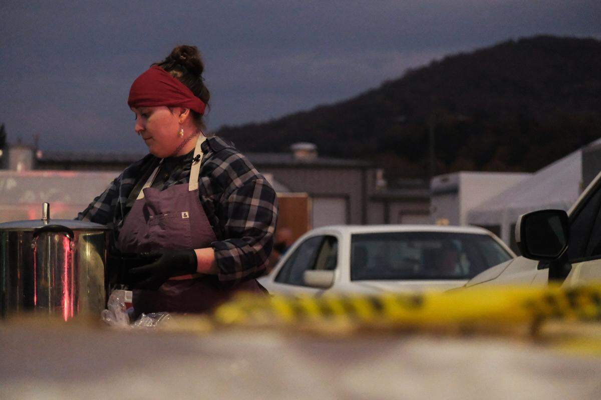 Cayte Gowan serves free meals to residents in need in the Ingles parking lot in Swannanoa, N.C., on Oct. 26, 2024. Framed by the mountains at dusk, Gowan has been working from early morning well into the evening.