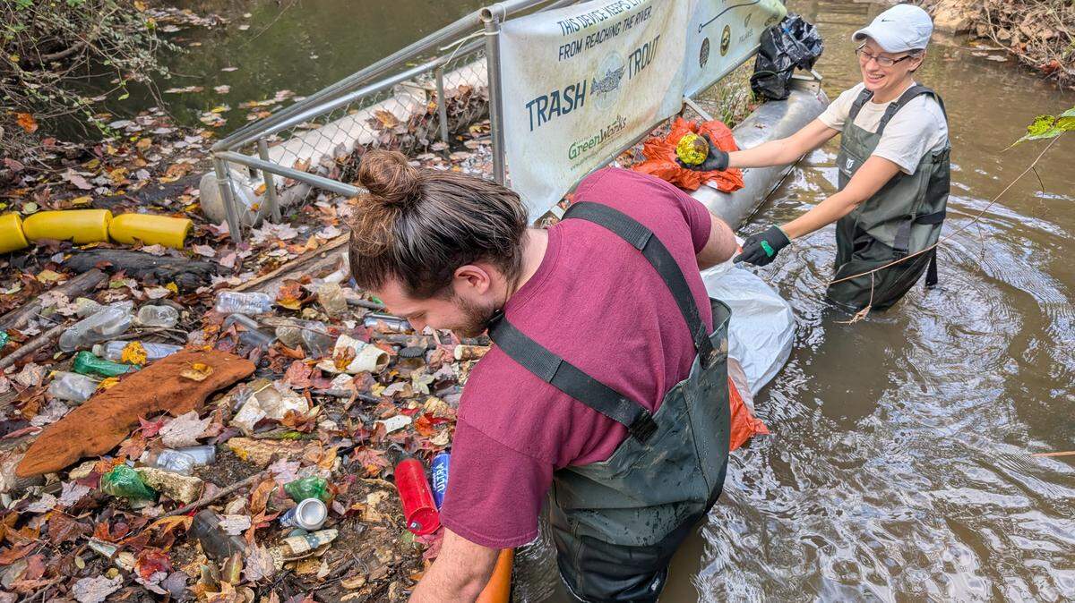 Two volunteers with Haw River Assembly, Halle Amick and Chris Preheim., cleaning out a trash trap installed on Third Fork Creek in Durham on October 26, 2024.