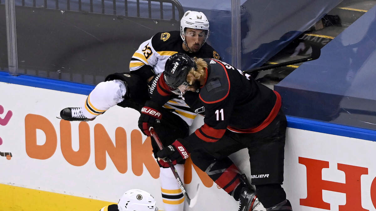 Boston Bruins left wing Brad Marchand (63) checks Carolina Hurricanes center Jordan Staal (11) during first-period NHL Eastern Conference Stanley Cup playoff hockey action in Toronto, Monday, Aug. 17, 2020. (Nathan Denette/The Canadian Press via AP)