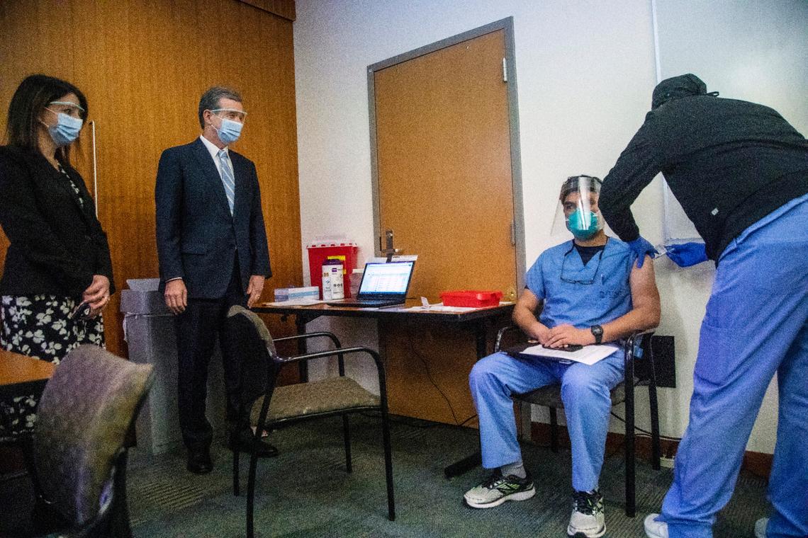Secretary of the NC Department Health and Human Services Dr. Mandy Cohen and Gov. Roy Cooper, at left, watch as Dr. Aidin Ashoori, receives a COVID-19 vaccine from LPN Gerda Lambre at UNC Health in Chapel Hill, NC Thursday, Dec. 7, 2020 where frontline healthcare workers are among some of the first recipients of the Pfizer COVID-19 vaccine.