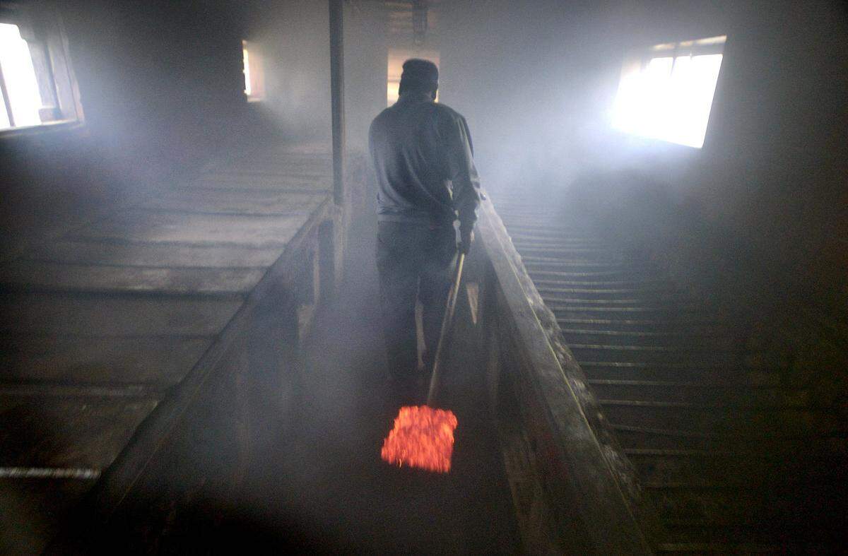 A shovel full of glowing hardwood coals is carried through the smoke-filled cookhouse at Wilber’s Barbecue in Goldsboro. The first rays of morning sunlight filter through the smoke as he fires the barbecue pit of slow-cooking pigs for the last time that day after cooking the pigs through the night.