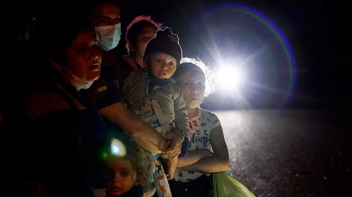 In this May 17, 2021 file photo, a group of migrants mainly from Honduras and Nicaragua wait along a road after turning themselves in upon crossing the U.S.-Mexico border, in La Joya, Texas. On Jan. 2, 2022, the number of migrant children in federal custody fell​ below 10,000 for the first time since last March.
