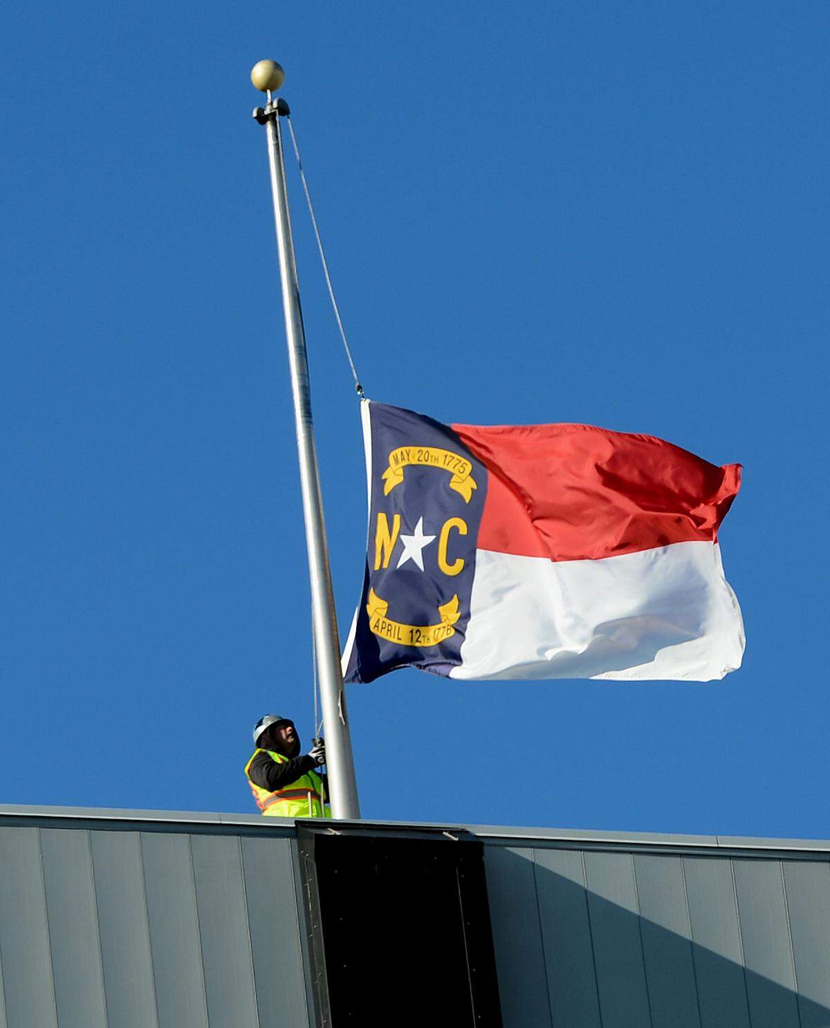 A construction worker lowers the North Carolina state flag from atop Bank of America Stadium on Thursday, January 16, 2014.