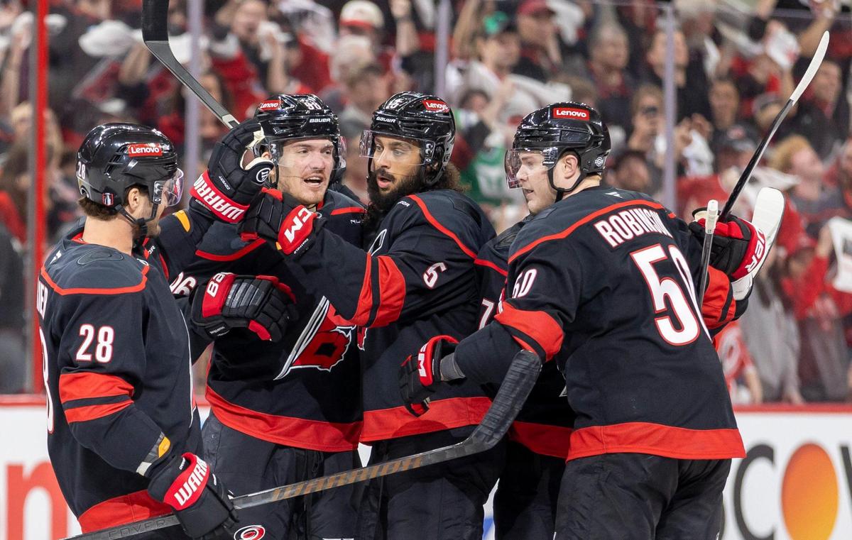 Carolina Hurricanes defenseman Jalen Chatfield (5) is surround by teammates William Carrier (28), Jack Roslovic (96) and Eric Robinson (50) after he scored to give the Hurricanes a 1-0 lead against the New Jersey Devils in the first game of the playoffs on Sunday, April 20, 2025 at Lenovo Center in Raleigh, N.C.