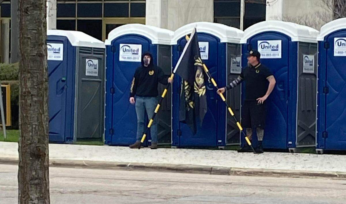 Two men in Proud Boys uniform stand guard over a portable toilet in downtown Raleigh Friday. About 40 people joined their protest.