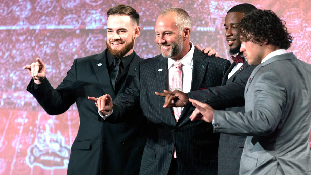 N.C. State quarterback Devin Leary, head coach Dave Doeren and linebackers Isaiah Moore and Drake Thomas flash the Wolfpack sign prior to meeting with the media during the 2022 ACC Football Kickoff on Wednesday, July 20, 2022 in Charlotte, N.C.