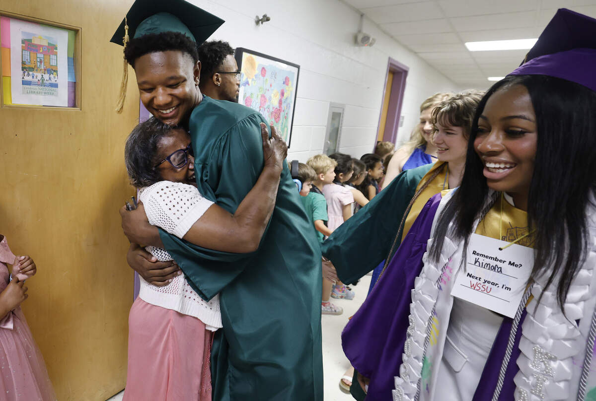 Enloe senior Elijah Jeffreys hugs Gwen “Grandma Gwen” Strokes as former students, now graduating high school seniors, walk the halls of Powell Elementary in Raleigh on Wednesday. Kimora Winters walks to the right.