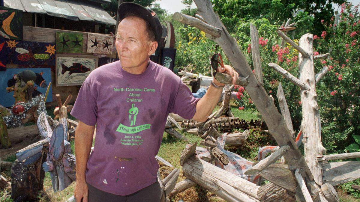Chainsaw sculptor Clyde Jones stands with some of his cedar creations and hand paintings, (background) around his home in the small Chatham County mill town of Bynum.