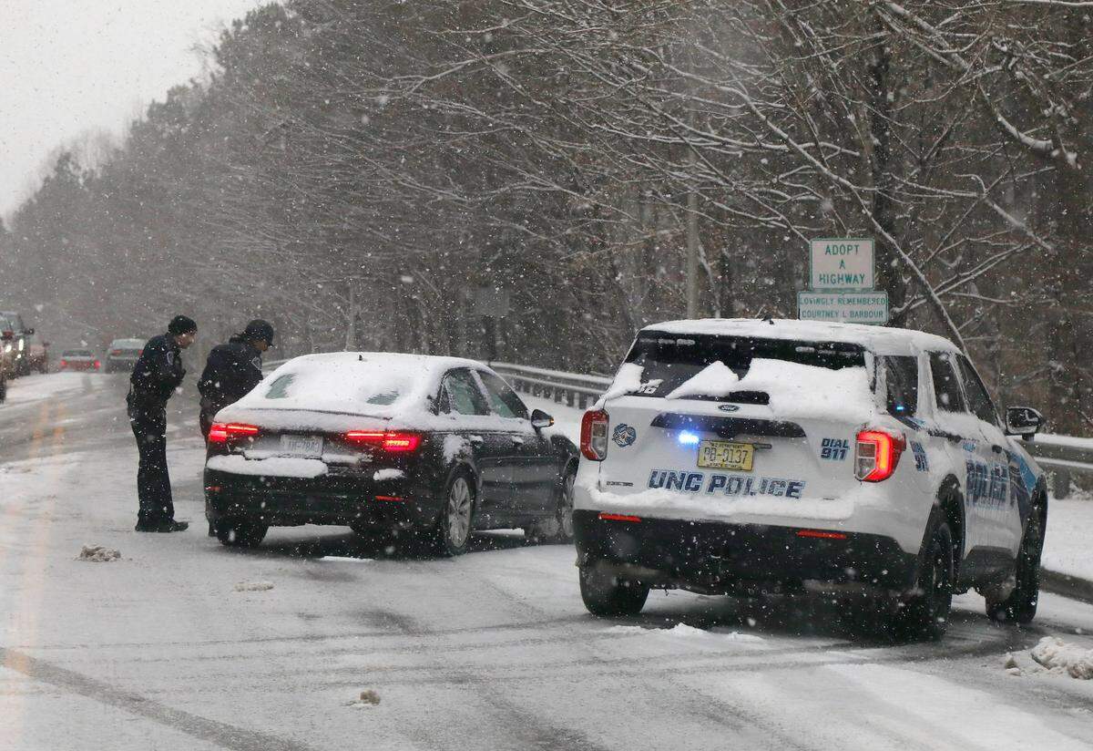 Law enforcement officers help a stalled vehicle on Manning Drive as snow falls in Chapel Hill, N.C. on Wednesday, Feb. 19, 2025.