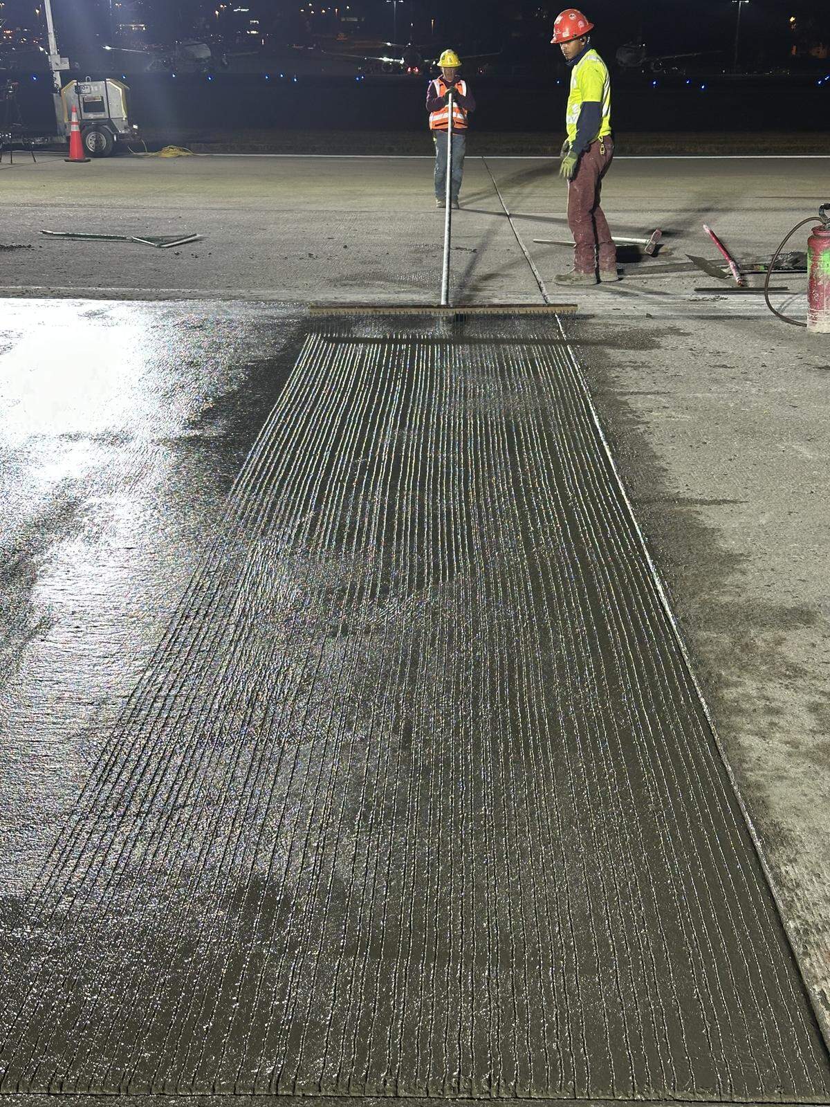 A Hi-Way Paving employee uses a rake to etch grooves in the wet concrete on runway 5L/23R at Raleigh-Durham International Airport on Oct. 20, 2025. The grooves help airplane tires better grip the runway.