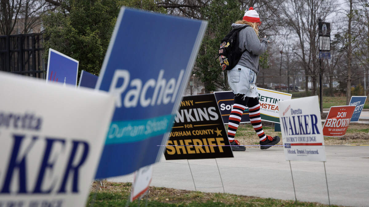 A person walks among campaign signs near the Durham County Main Library on Tuesday, March 3, 2026, in Durham, N.C.