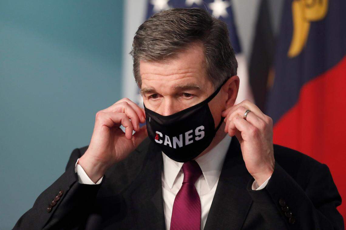 Gov. Roy Cooper prepares to take off his Canes mask before speaking during a briefing at the Emergency Operations Center in Raleigh, N.C., Wednesday, July 1, 2020.
