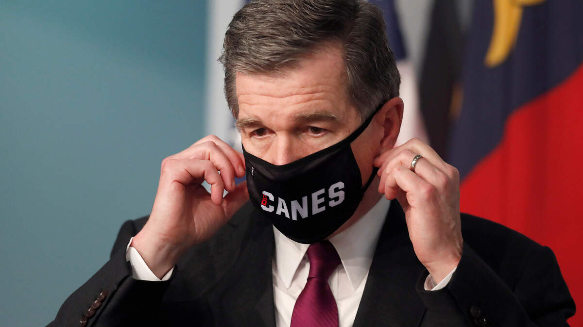 Gov. Roy Cooper prepares to take off his Canes mask before speaking during a briefing at the Emergency Operations Center in Raleigh, N.C., Wednesday, July 1, 2020.