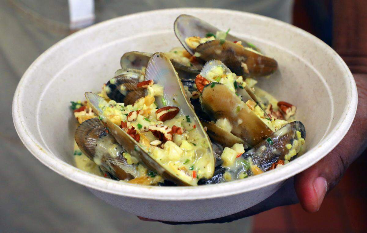 Ricky Moore, chef and owner of Saltbox Seafood Joint, holds a dish of North Carolina mussels braised in coconut cream with persimmon, apple and fried pecans at his restaurant in Durham, N.C. on Monday, Nov. 14, 2022. Moore is The News & Observer’s 2022 Tar Heel of the Year.