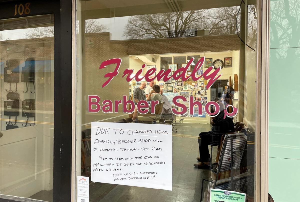 Owner Russ Sturdivant and barber Abe Thompson, seen through the storefront window, work with the last customers of the day at Friendly Barber Shop in Carrboro, NC.