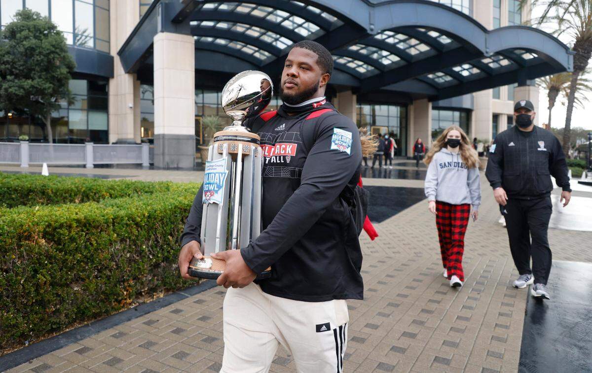 N.C. State center Grant Gibson carries the Holiday Bowl trophy as he and the N.C. State players, coaches and staff leave the team hotel to head to the airport in San Diego, CA Wednesday, Dec. 29, 2021.