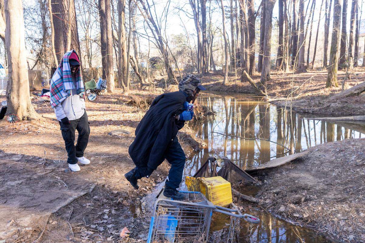 A woman who identified herself as “Sesame,” center, and a man who calls himself “Wiz” cross a makeshift bridge where they live in a tent next to the exit ramp from eastbound I-40 onto South Saunders Street in Raleigh.