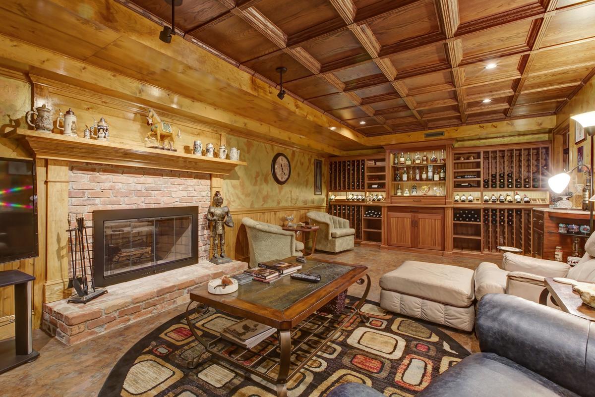 Creating a coffered ceiling in place of the old acoustic ceiling, adding a rustic wall finish, a custom wine cellar with a built-in humidor, and practical LVT flooring makes for a cozy basement wine cellar and cigar room.