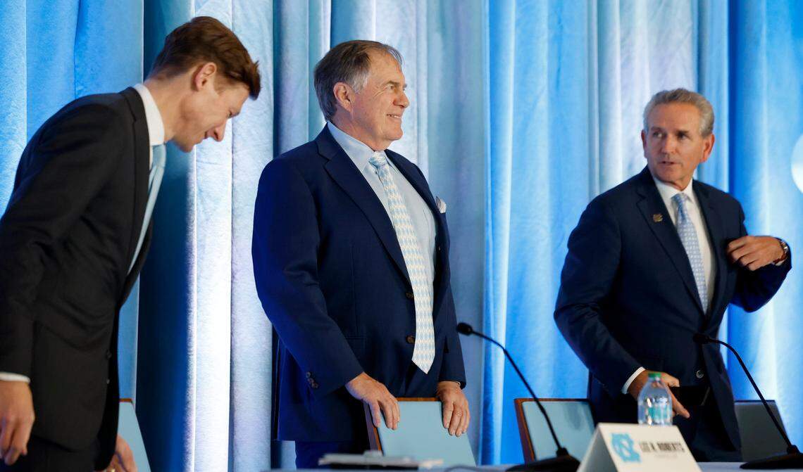 New North Carolina head football coach Bill Belichick prepares to sit at the start of the press conference announcing his hiring at the Loudermilk Center for Excellence at UNC in Chapel Hill, N.C., Thursday, Dec. 12, 2024. Chancellor Lee Roberts stands to the left and AD Bubba Cunningham stands to the right.