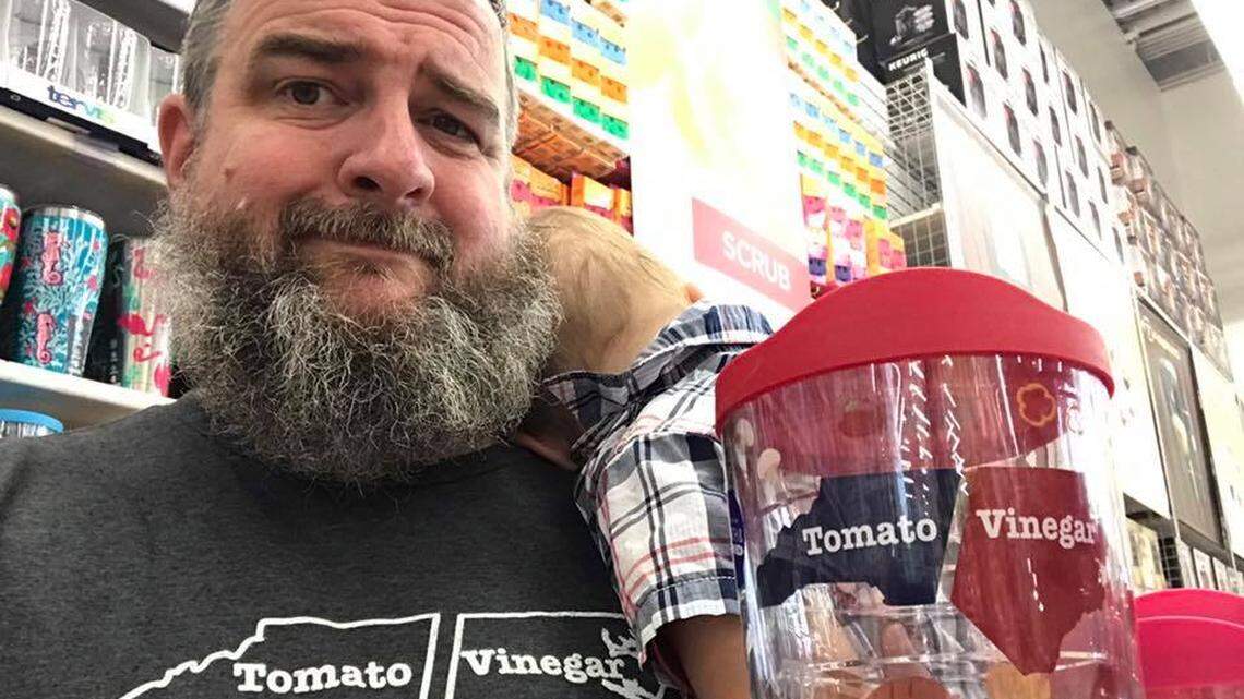 John Pugh, wearing his House of Swank design, and holding up a copy of that design on a Tervis tumbler sold at the Cary, North Carolina Bed, Bath and Beyond store.
