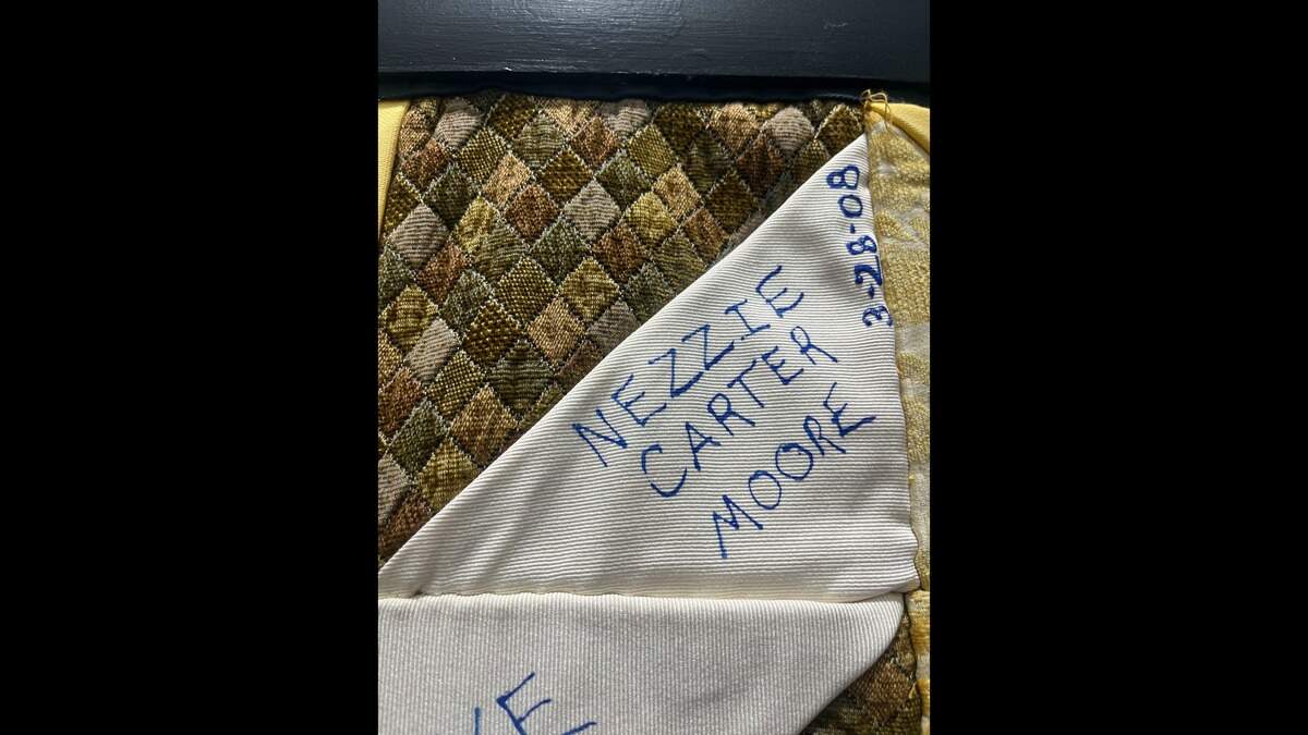 A square on the Durham Homicide Memorial Quilt, half of it white and half of it with green-and-brown diamonds like argyle, with the name of Nezzie Carter-Moore and the date when she was killed on the white half.