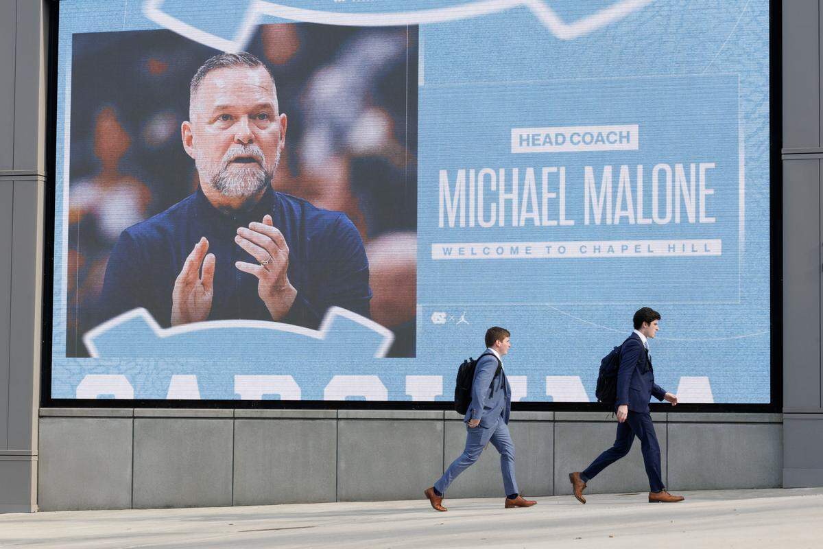 People walk by a photograph of North Carolina men’s basketball head coach Michael Malone prior to an introductory press conference at the Smith Center on Tuesday, April 7, 2026, in Chapel Hill, N.C. 
