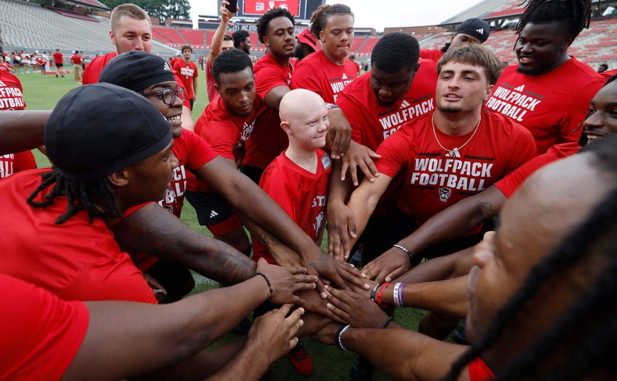 Luke Girardian and Wolfpack players bring their hands in to celebrate a touchdown during Victory Day at Carter-Finley Stadium in Raleigh, N.C., Friday, August 2, 2024. Victory Day is a partnership between the Wolfpack and GiGi’s Playhouse, a Down Syndrome achievement center in Raleigh. The event provided 52 cognitively and physically impaired people the chance to be football stars for the night. They tried on uniforms, met the players and coaches, ran through the tunnel and competed in drills with the players.