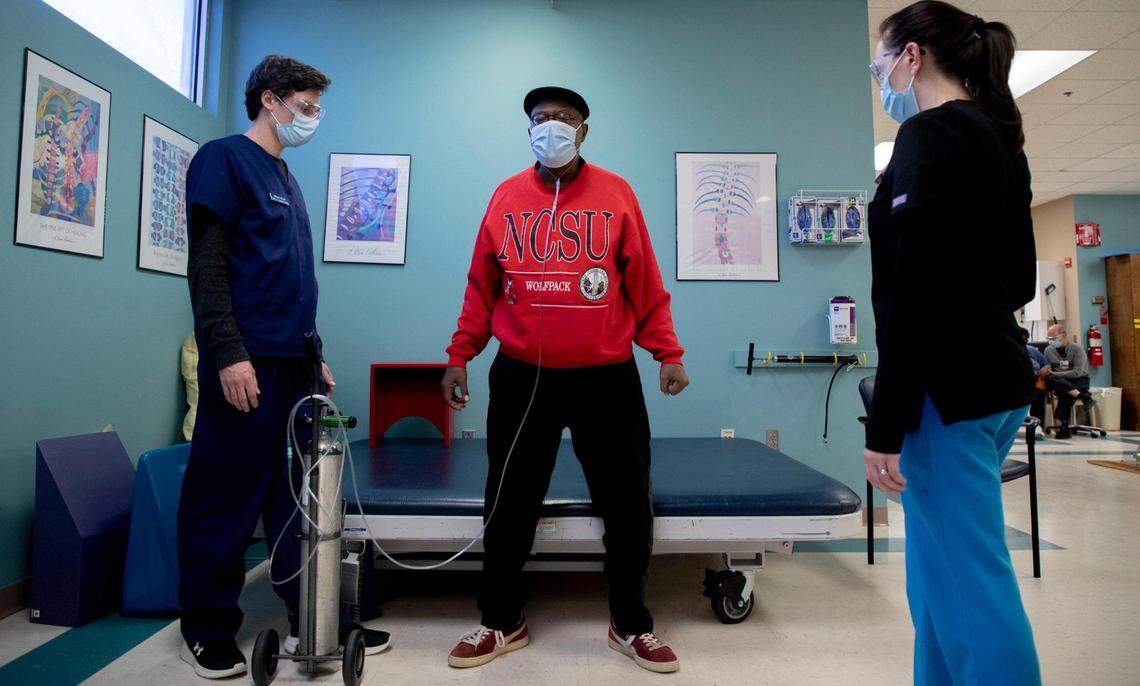 David McShaw, center, practices sitting and standing without using his arms during an outpatient rehabilitation session, to help him regain the strength and mobility he lost during the 49 days he spent at UNC Hospitals recovering from a severe COVID-19 infection, at Maria Parham Health, on Thursday, Nov. 19, 2020, in Henderson, N.C.