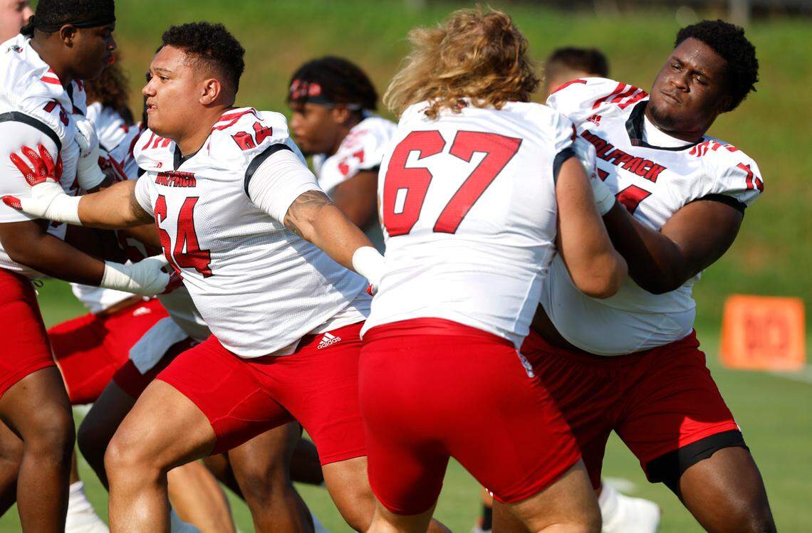 N.C. State’s Chandler Zavala (64), left, and Anthony Belton (74) block while drilling during the Wolfpack’s first practice of fall camp in Raleigh, N.C., Wednesday, August 3, 2022. Belton is blocking Brendan Lawson (67).