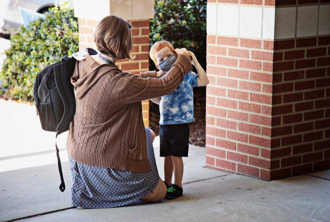 A school employee helps a young student with his mask at Carpenter Elementary School in Cary on Thursday morning, Aug. 19, 2021. North Carolina students will start their third school year dealing with the coronavirus pandemic just as the highly contagious delta variant is rapidly spreading across the state.
