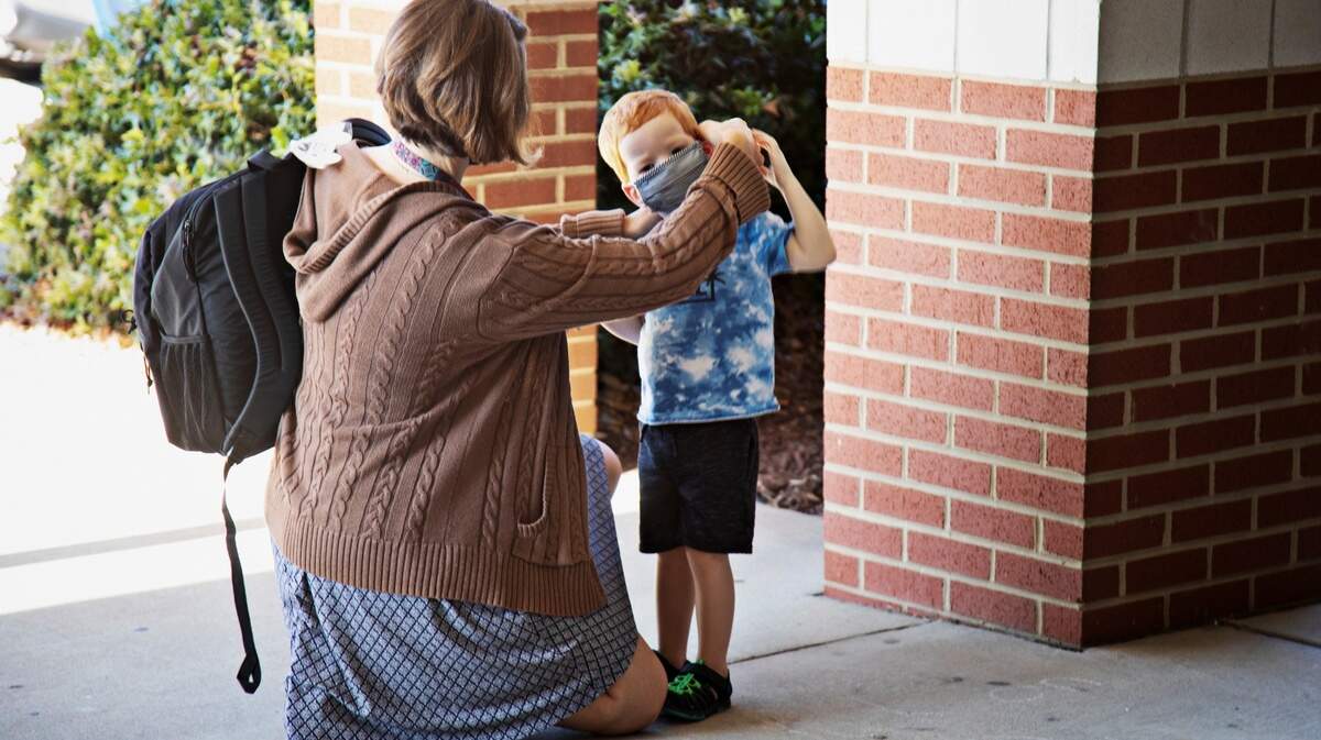 A school employee helps a young student with his mask at Carpenter Elementary School in Cary on Thursday morning, Aug. 19, 2021.