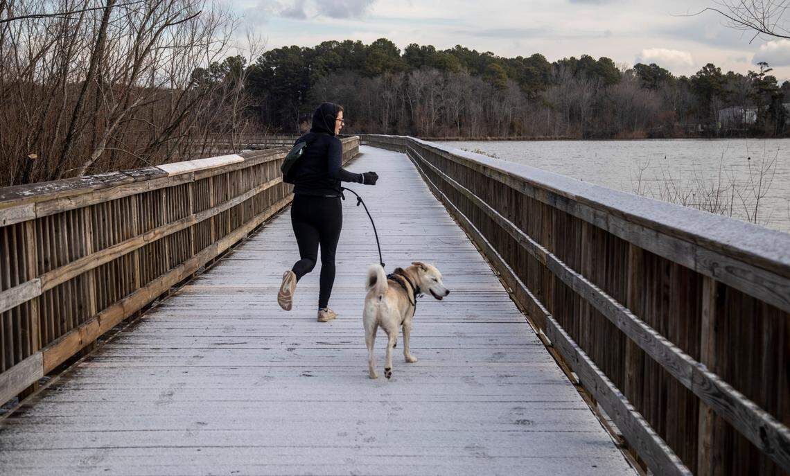 Elyse Groffin and her dog Haku run along Crabtree Creek Trail in Raleigh after a light dusting of snow accumulated on the boardwalk structures on the trail Saturday morning, Jan. 29, 2022.