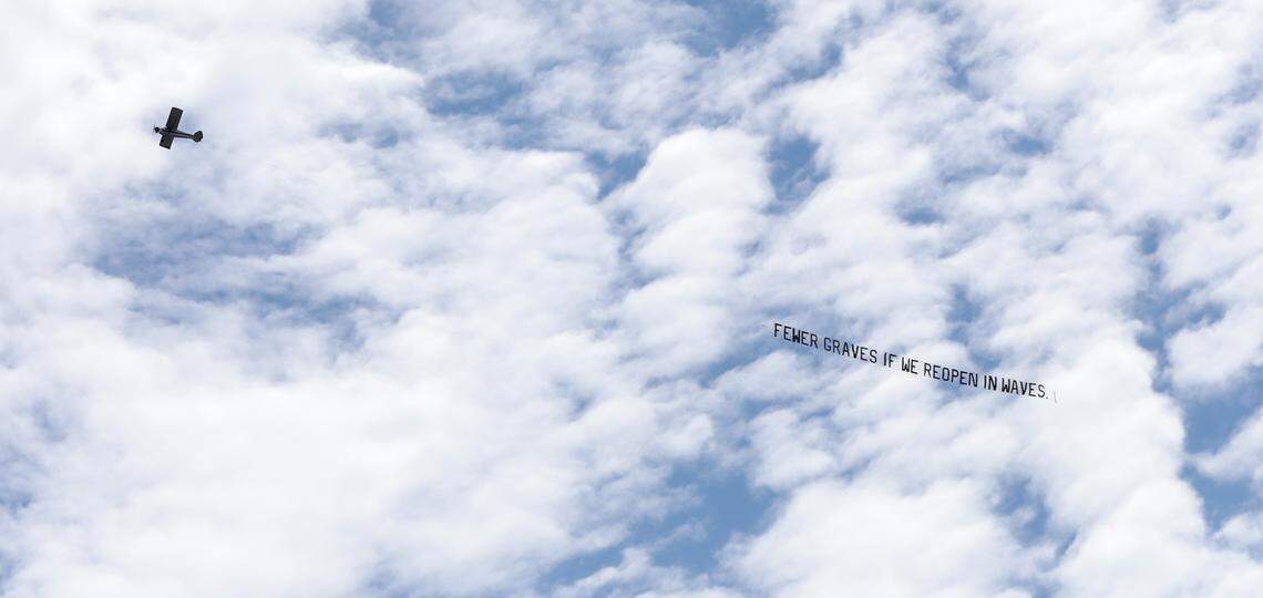 A plane, with a counter protest message, circles over the ReOpenNC protest in downtown Raleigh, N.C., Tuesday, May 12, 2020.