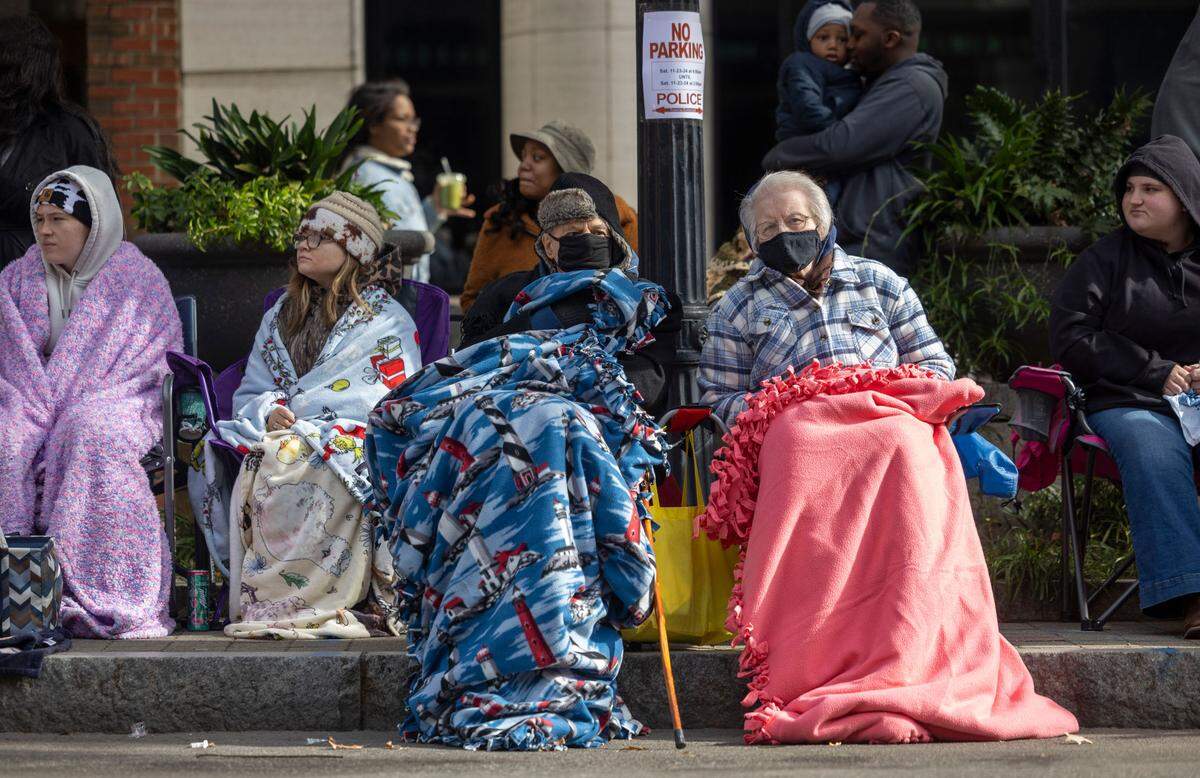 Parade attendees are wrapped up on a chilly morning in the shade of a building along Fayetteville Street, during the 80th annual Raleigh Christmas Parade on Saturday, November 23, 2024 in Raleigh, N.C.
