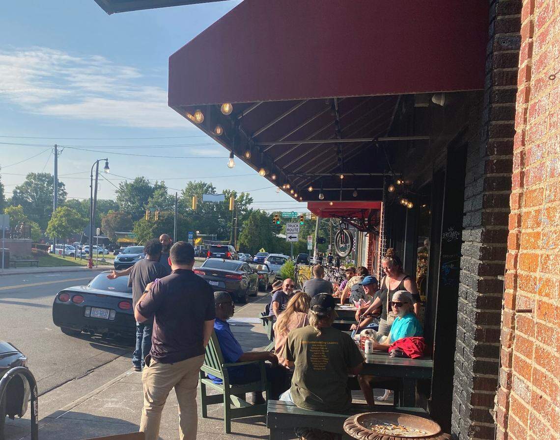 People sitting in the sun outside Dain’s Place on 9th Street in Durham.